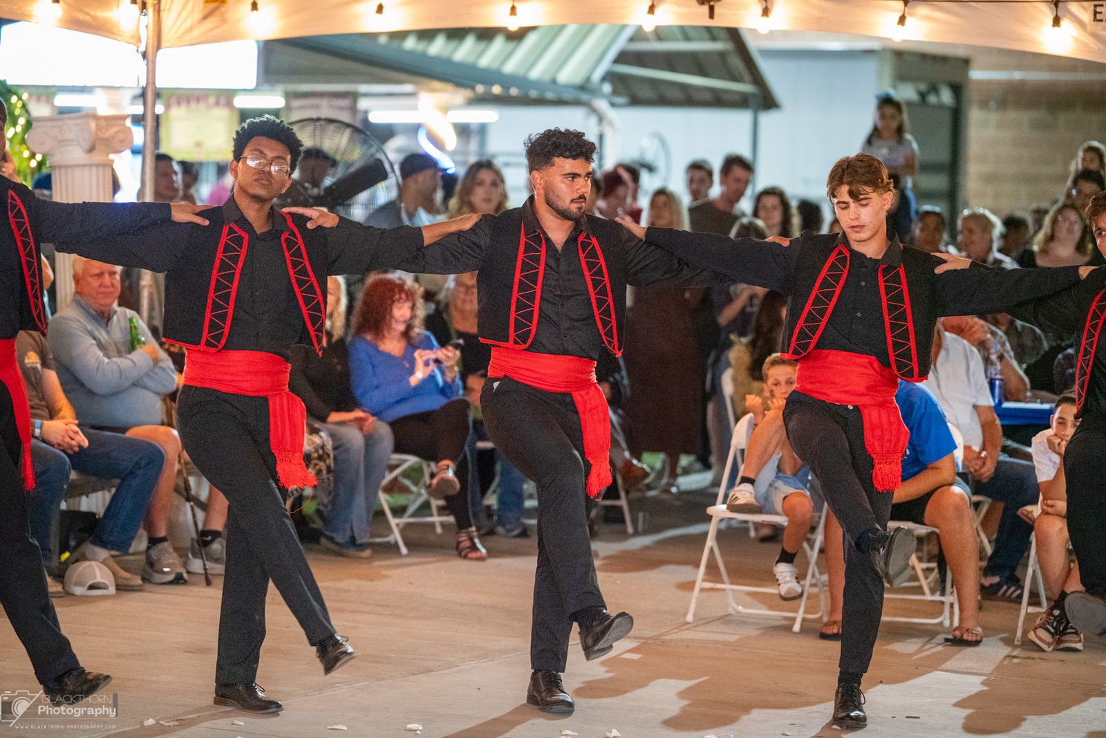 Men in black vests and red sashes kicking in a line under the tent